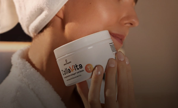 Frau mit weißem Handtuch auf dem Kopf hält Kollagen-Supplement-Glas nah an ihrem Gesicht