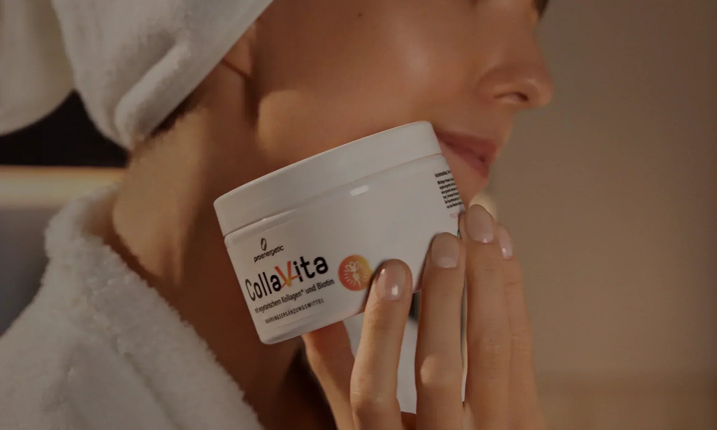 Frau mit weißem Handtuch auf dem Kopf hält Kollagen-Supplement-Glas nah an ihrem Gesicht