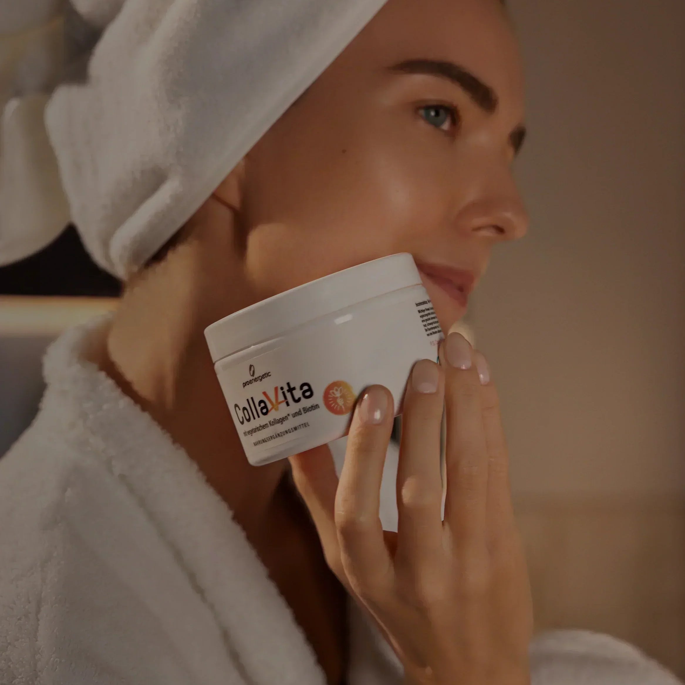 Frau mit weißem Handtuch auf dem Kopf hält Kollagen-Supplement-Glas nah an ihrem Gesicht