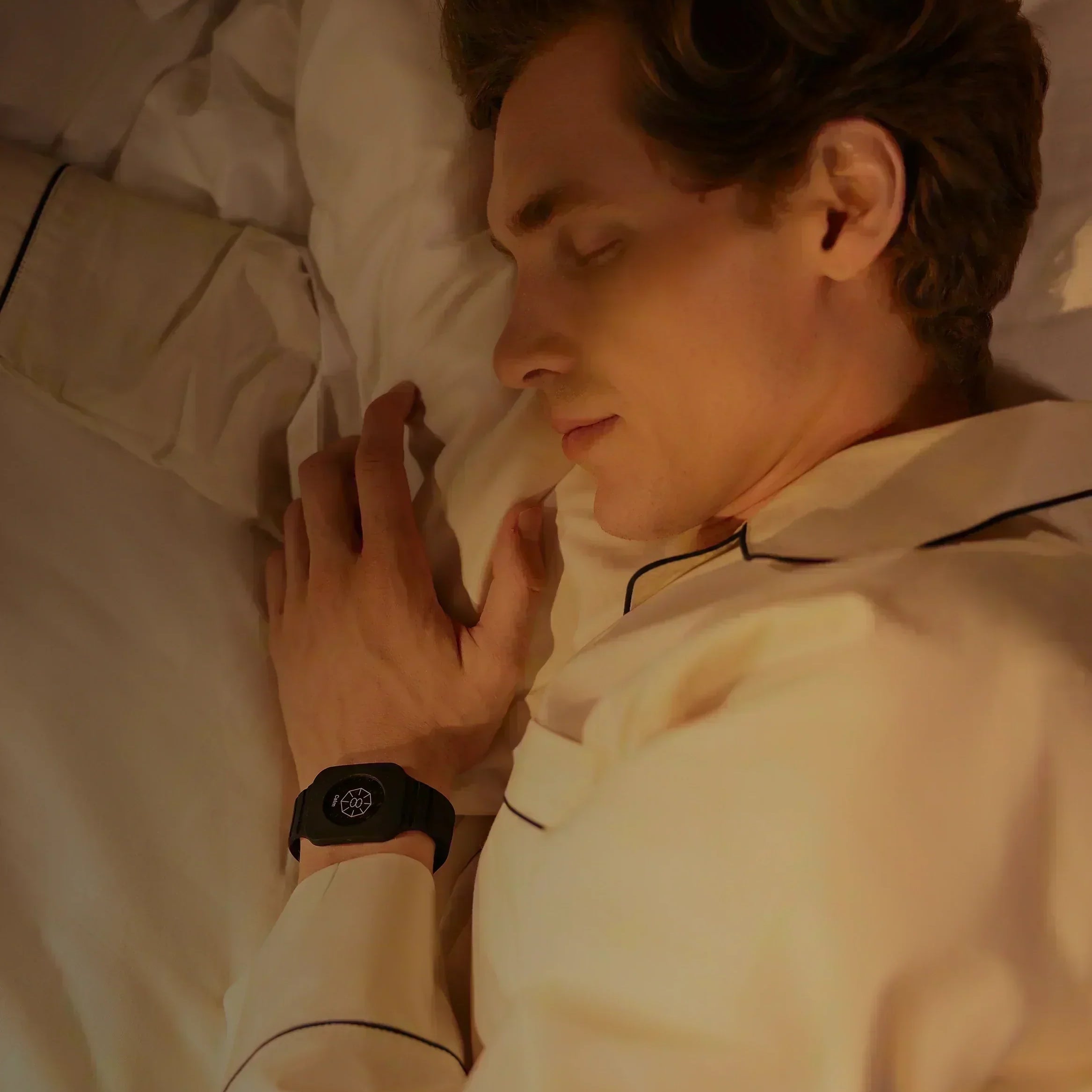 Mann liegt schlafend im Bett bei warmem Licht mit geschlossenem Augen und trägt Eloop Band mit Calm Chip am Handgelenk