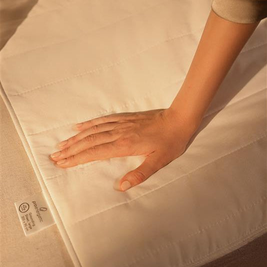 Hand liegt auf Grounding Matte am Bett in warmem Licht als Nahaufnahme