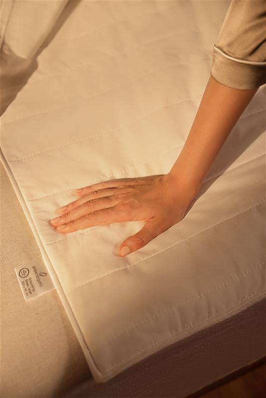 Hand liegt auf Grounding Matte am Bett in warmem Licht als Nahaufnahme