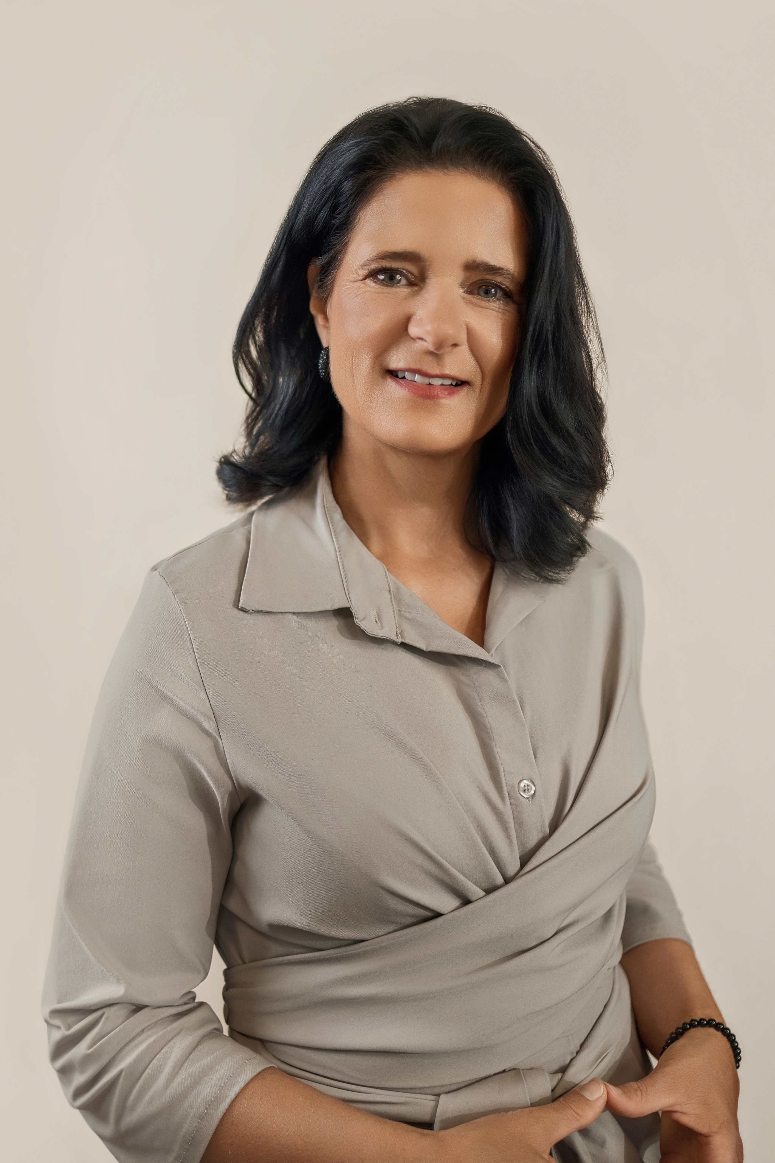 Porträt einer Frau mit dunklem schulterlangem Haar in heller Bluse vor neutralem Hintergrund