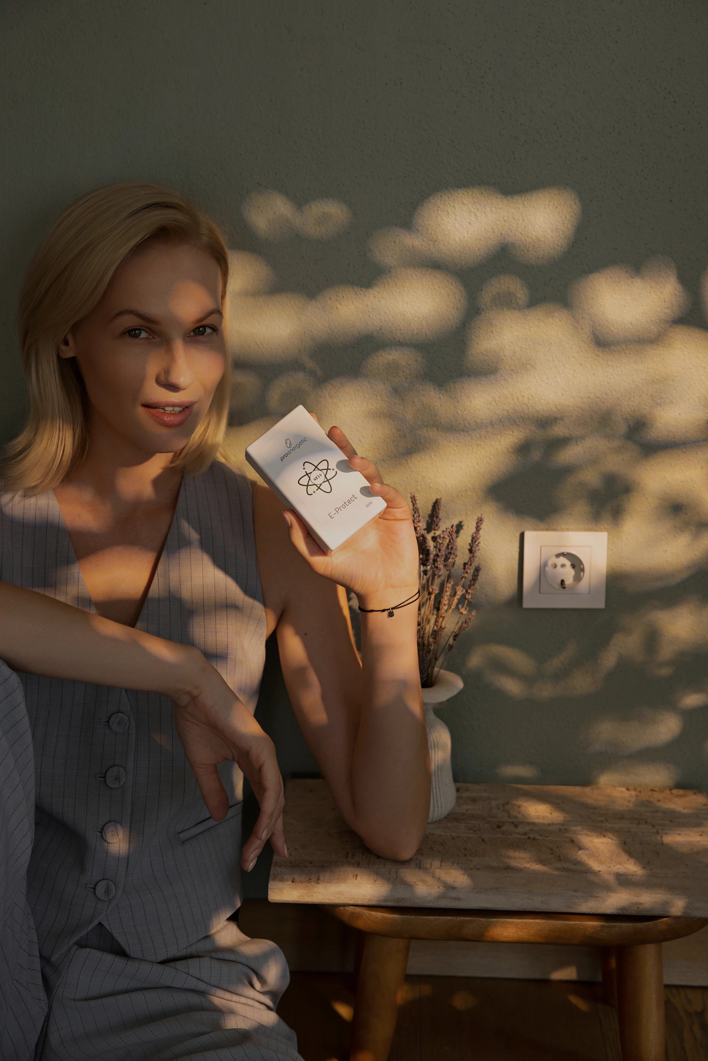 Frau sitzt an einem Tisch im Innenraum und hält das weiße ProEnergetic E-Protect S230 Steckgerät in der Hand