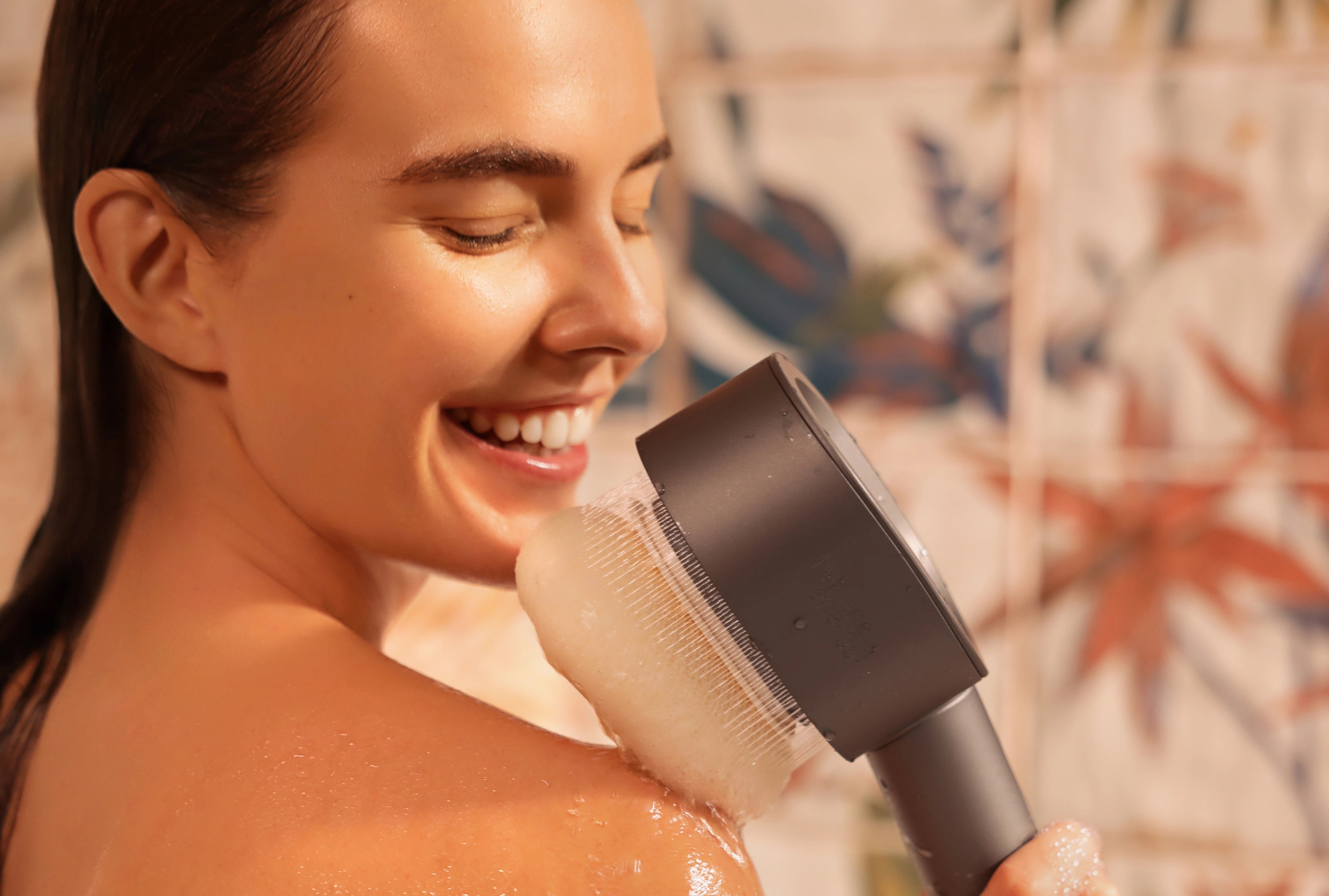 Person duscht im Badezimmer und hält den AERO Shower Duschkopf mit Peeling-Aufsatz an die Schulter, Haut ist nass und glänzend