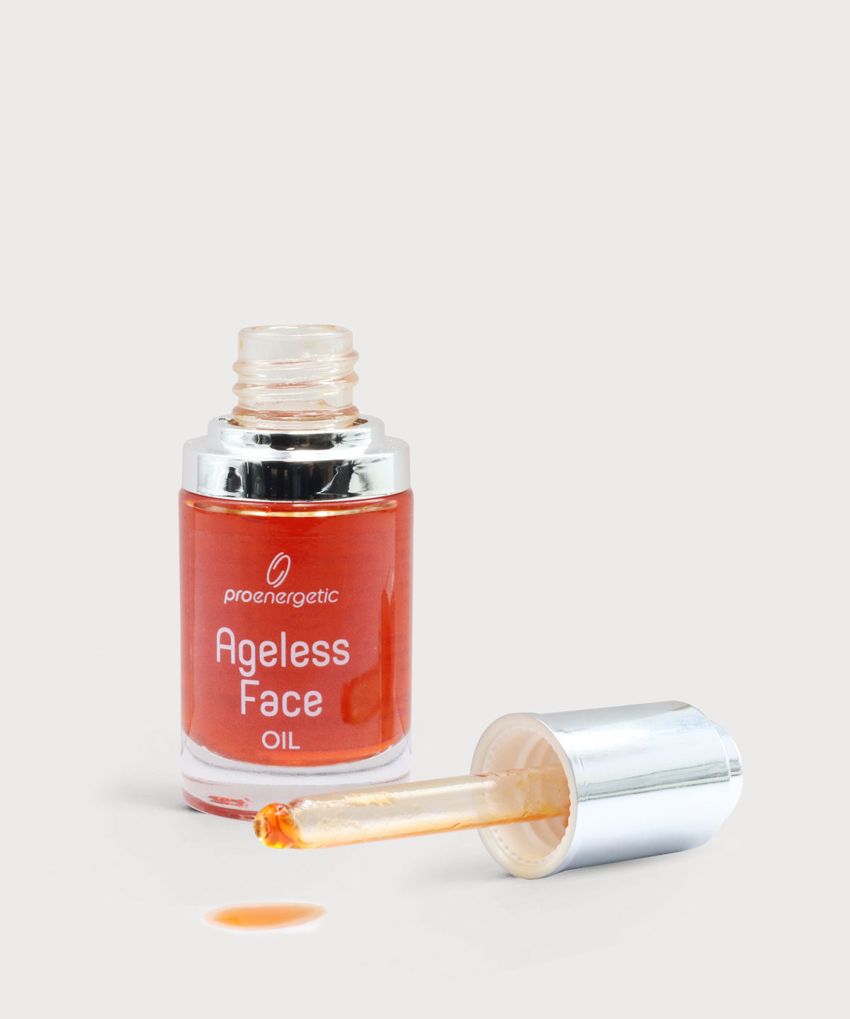Offene Glasflasche „Ageless Face Oil“ mit silberner Pipette, orangefarbenes Gesichtsöl sichtbar, ein Tropfen Öl auf hellem, neutralem Untergrund.