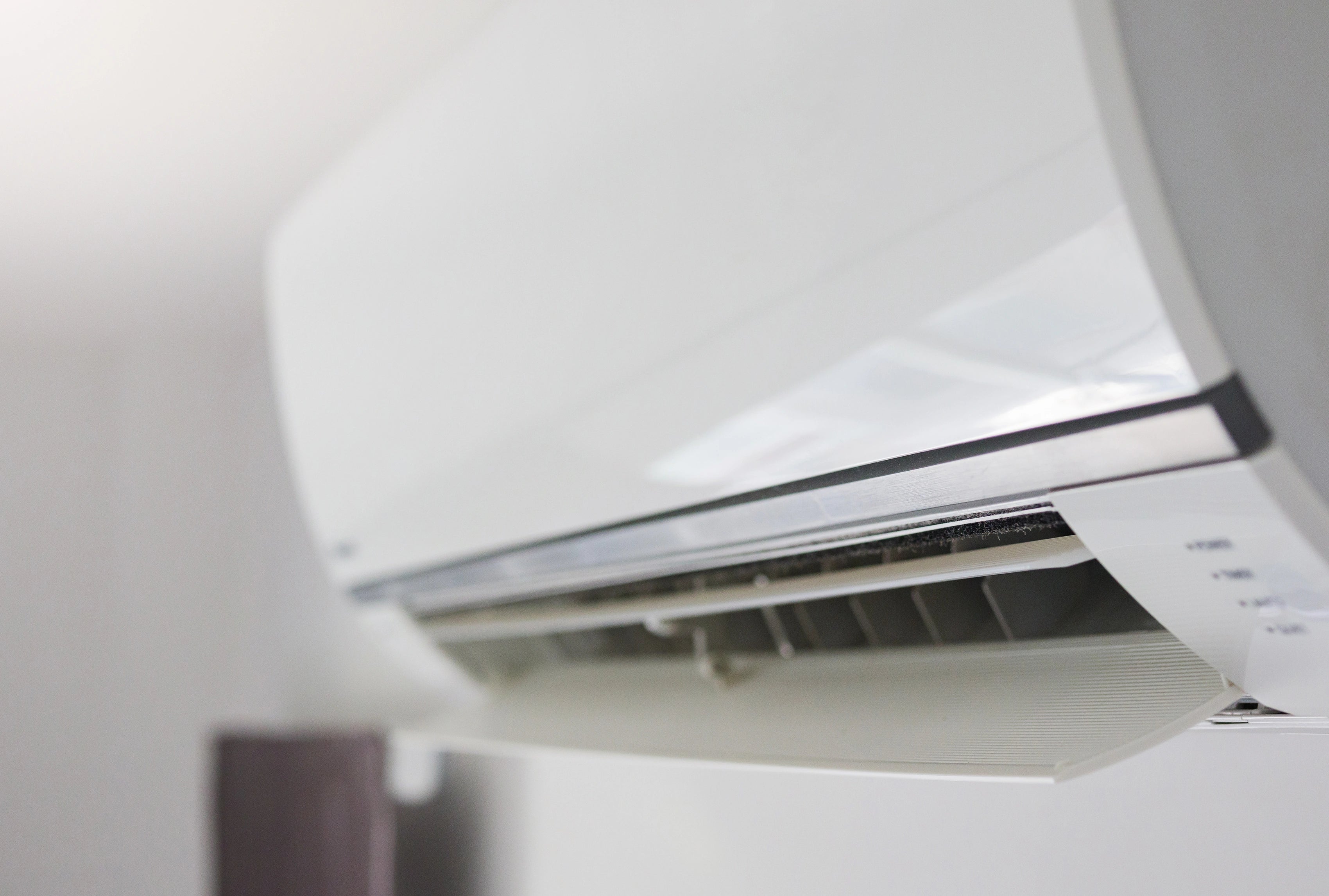 Wandmontierte Klimaanlage in Nahaufnahme mit geöffnetem Luftauslass in einem hellen Innenraum