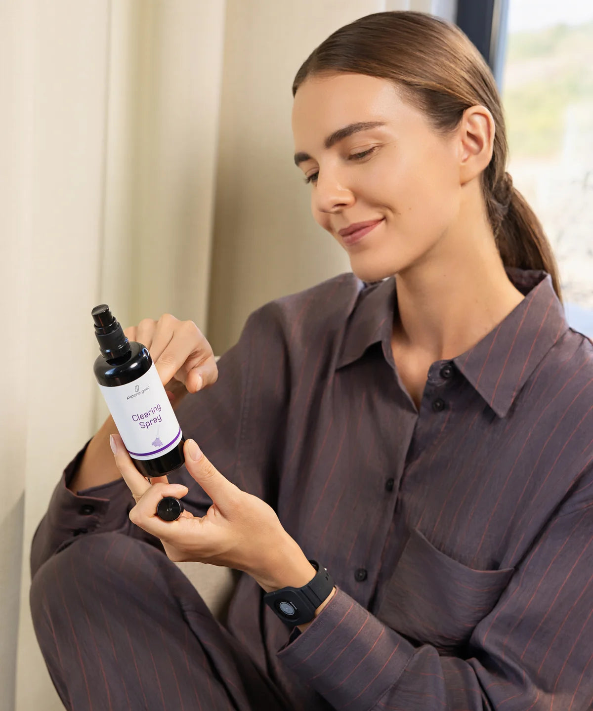 Person sitzt in einem Innenraum und betrachtet eine geöffnete Sprayflasche mit der Aufschrift Clearing Spray in den Händen