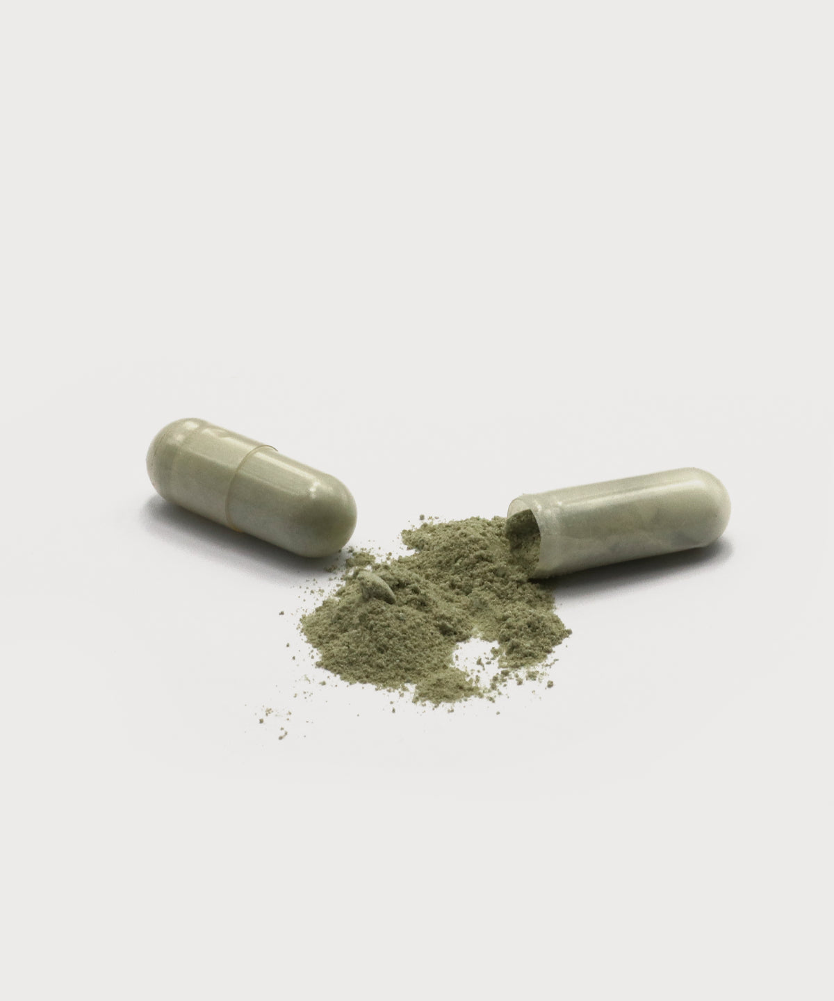 D-Tox Intense Caps. Eine geöffnete Kapsel mit grünlichem Pulver auf hellem Hintergrund, eine Kapsel liegend neben dem Inhalt.