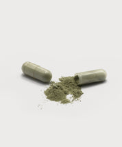 D-Tox Intense Caps. Eine geöffnete Kapsel mit grünlichem Pulver auf hellem Hintergrund, eine Kapsel liegend neben dem Inhalt.