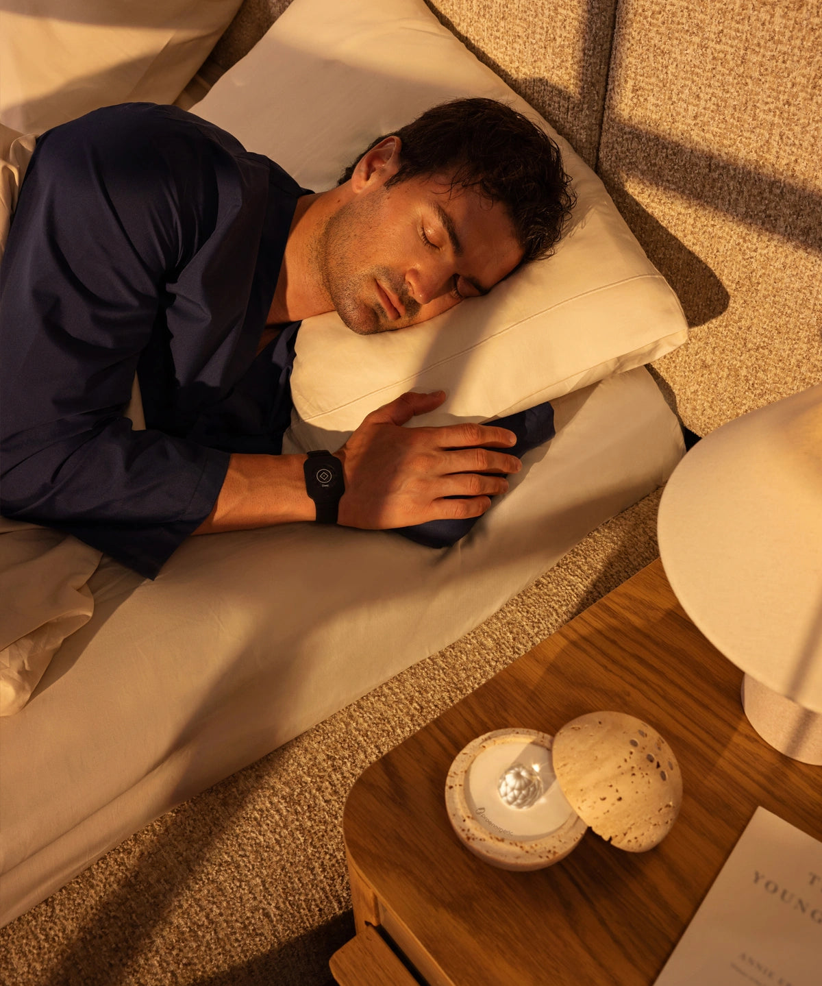 Man sleeping peacefully on his side in bed wearing a Eloop Band on his wrist, with the Dormea on the bedside table.