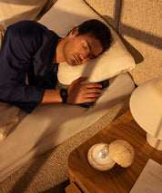 Man sleeping peacefully on his side in bed wearing a Eloop Band on his wrist, with the Dormea on the bedside table.