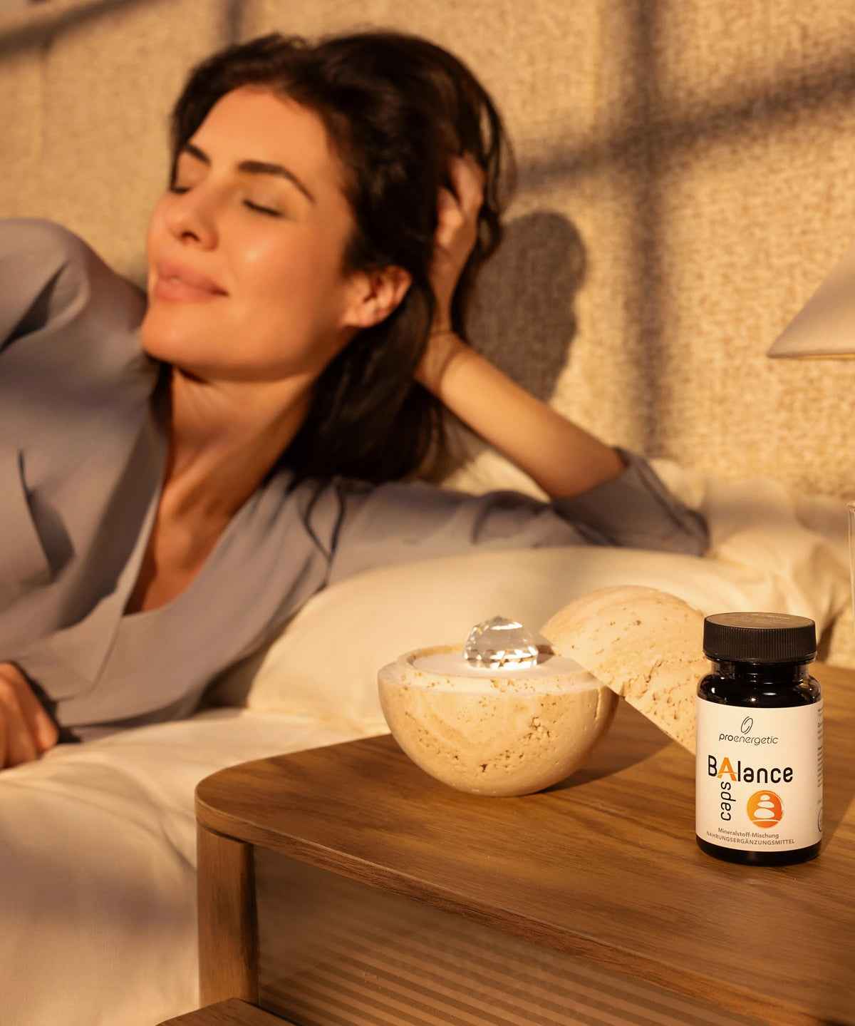 Woman relaxing in bed beside Dormea and ProEnergetic Balance Caps supplement on a bedside table.