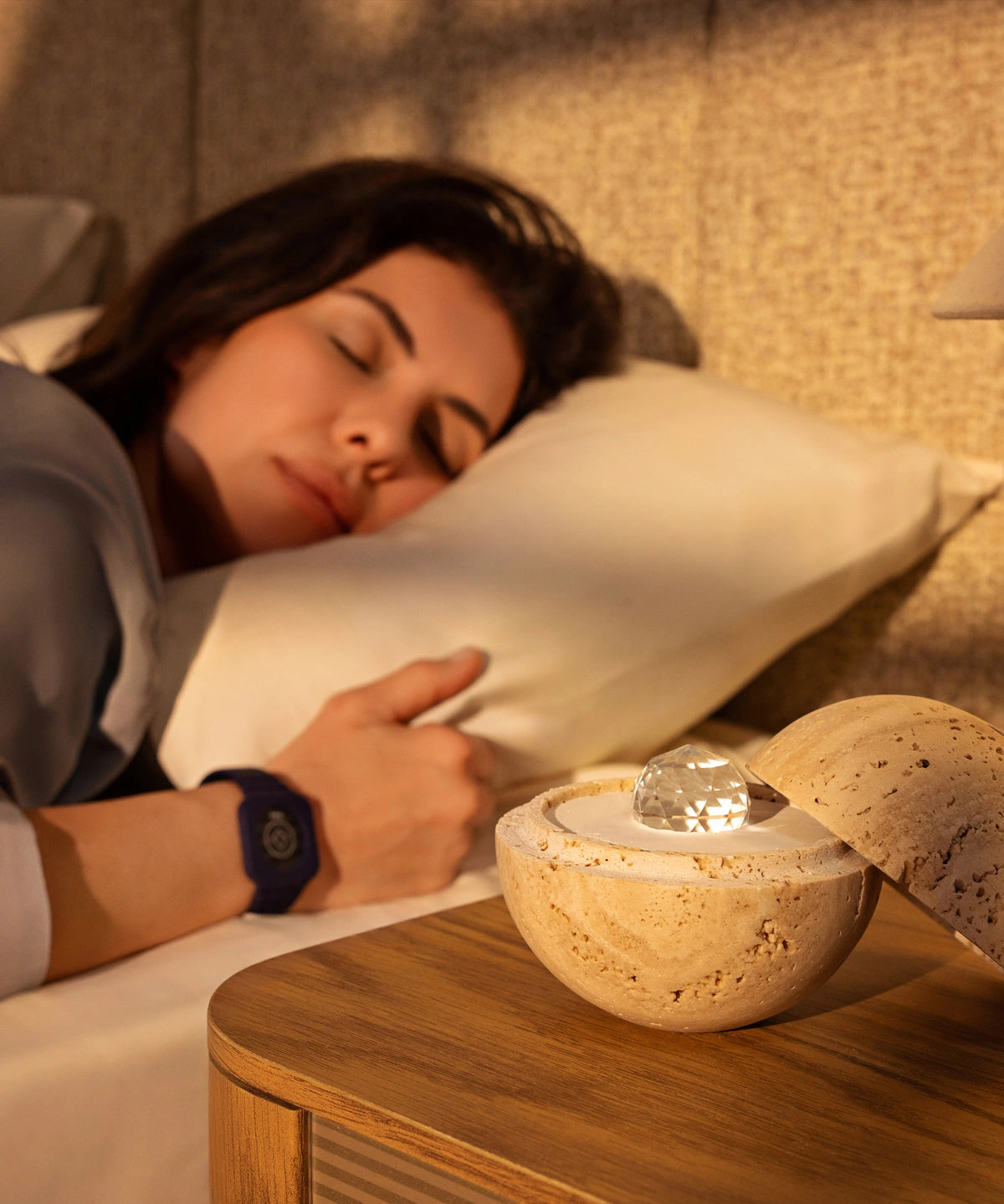 Woman sleeping peacefully while wearing the Eloop Band with sleep Chip, with the Dormea natural sand stone standing on the bedside table.