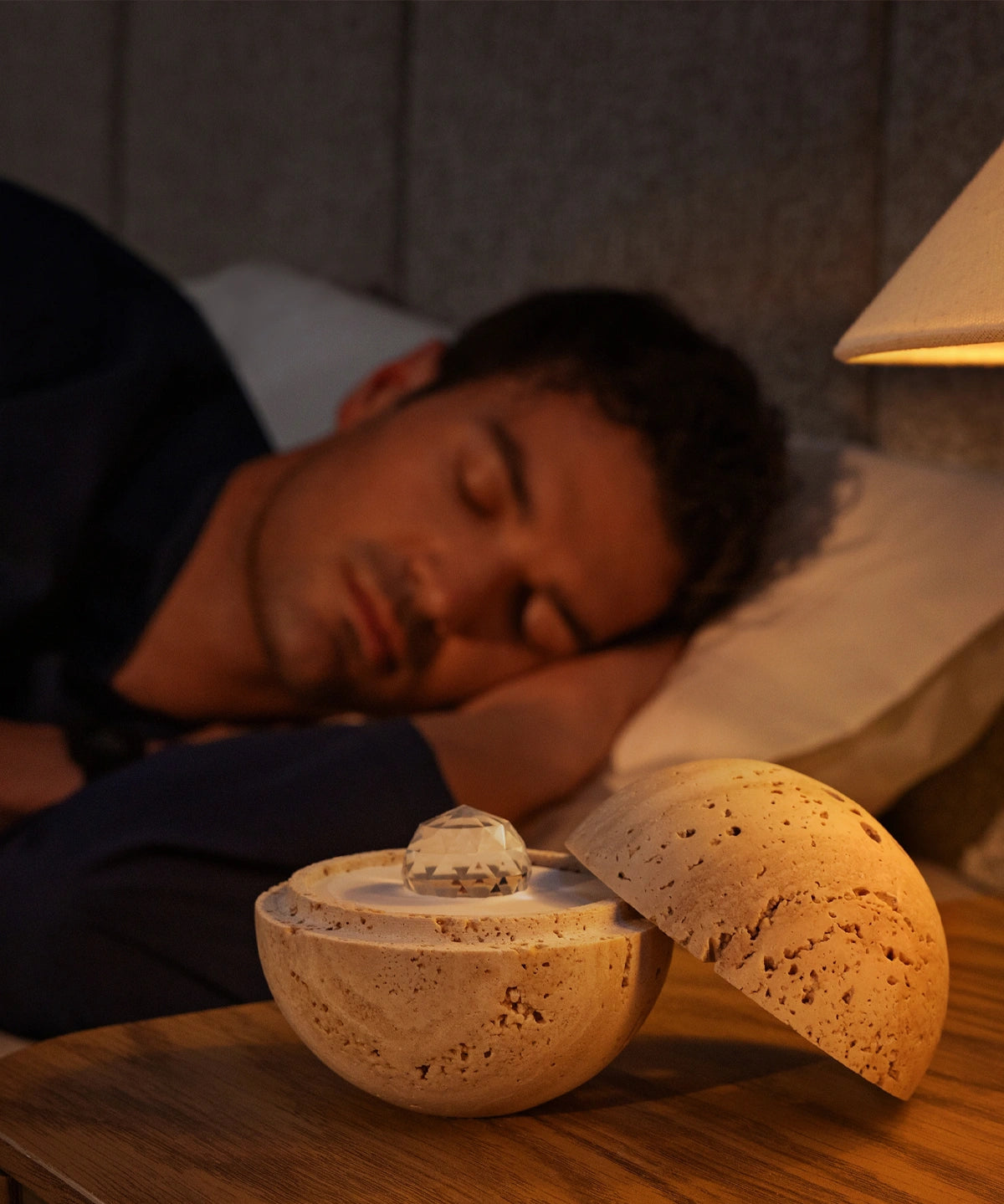 Dormea on its sand stone on a bedside table, with a man sleeping peacefully in the background.