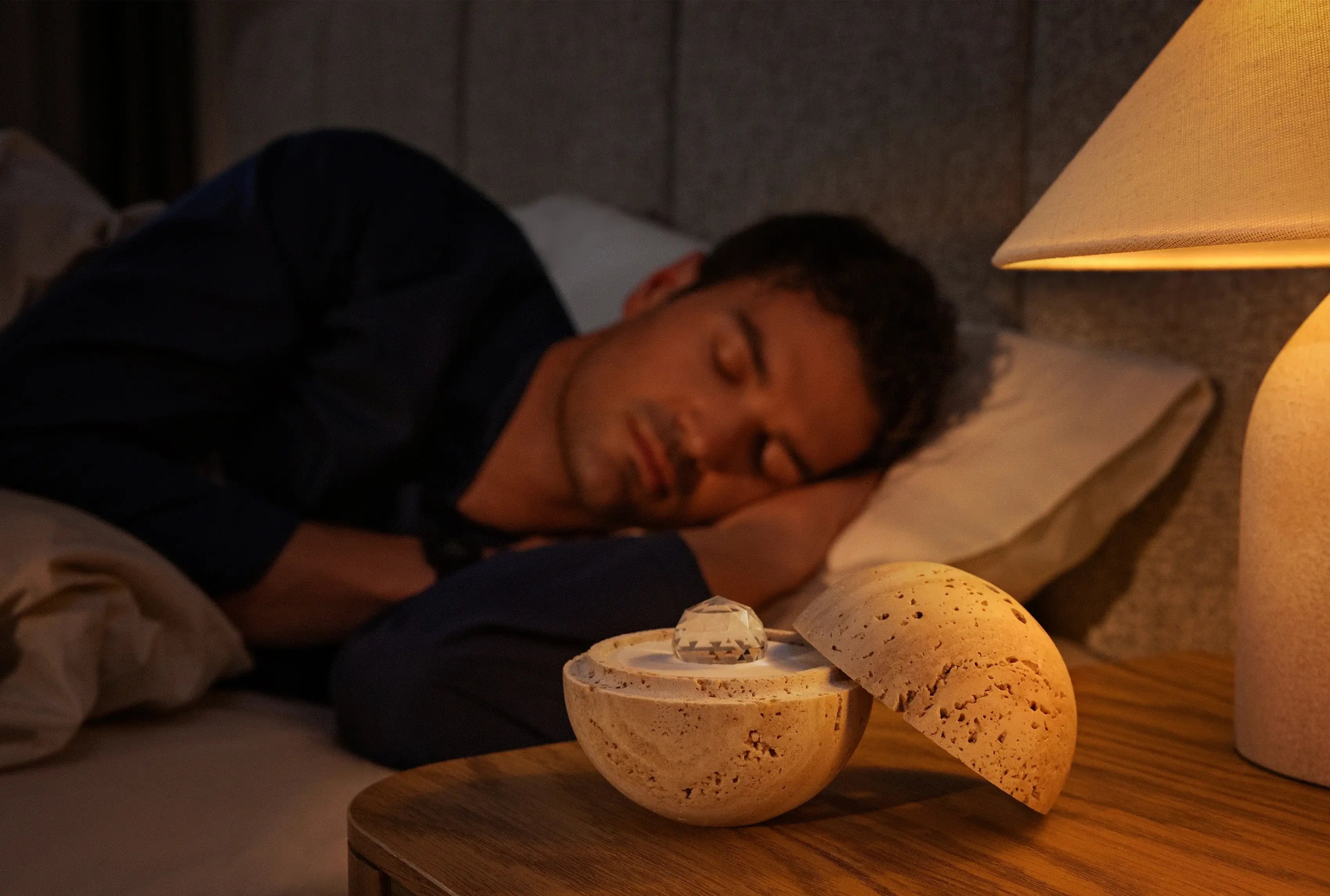 Dormea auf einem Nachttisch neben einem Mann, der friedlich im Bett schläft, im warmen Abendlicht.