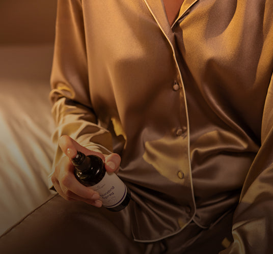 Person in satin shirt holding grounding spray bottle while seated indoors