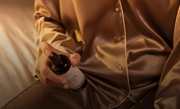 Person sitzt auf dem Bett und hält das Grounding Spray in der Hand, richtet den Sprühkopf auf den Fuß in ruhiger Umgebung