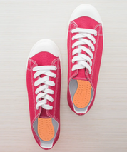 Rote Sneaker von oben gesehen, in beiden Schuhen liegen orangefarbene Footdoc Insoles MOVE | BALANCE Einlegesohlen; die MOVE-Seite der Einlagen zeigt nach oben.