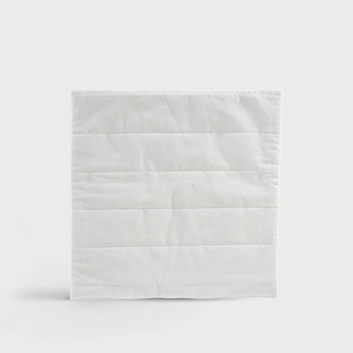 Quadratisches Grounding Relax Pad in weißer Textiloptik mit horizontalen Steppnähten auf neutralem Hintergrund