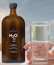 Braune Glasflasche H2O Fit von ProEnergetic neben gefülltem Wasserglas in einer Hand vor hellem Hintergrund.
