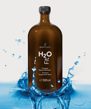 Braune Glasflasche H2O Fit von ProEnergetic mit schwarzem Schraubverschluss in spritzendem Wasser auf hellem Hintergrund.