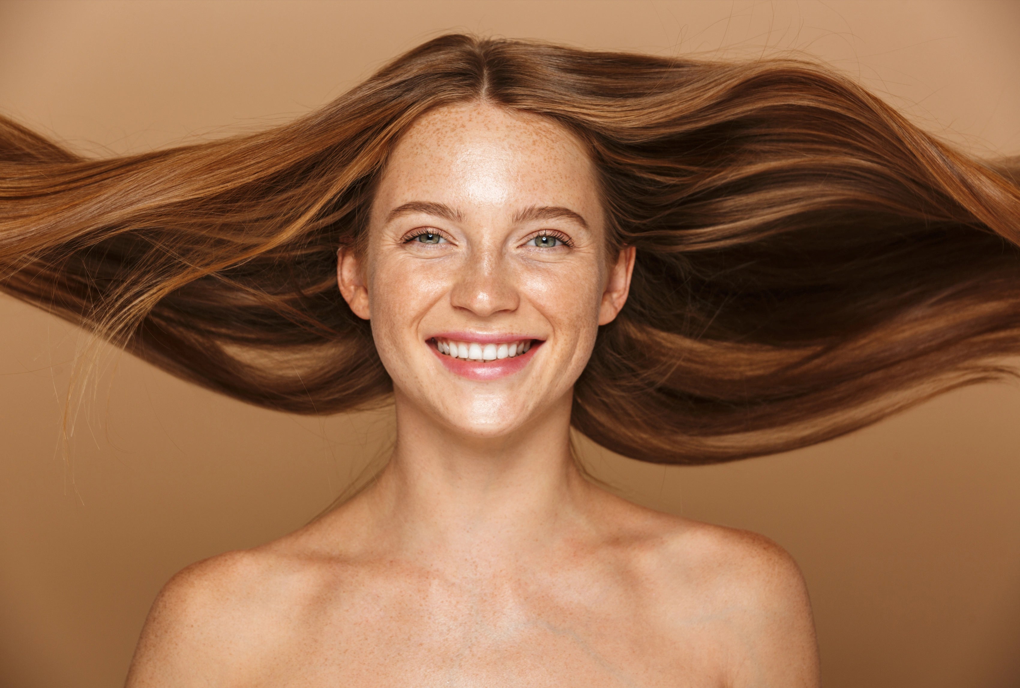 Lächelnde Frau mit gesund glänzendem, kraftvoll schwingendem Haar vor warmem Hintergrund – als visuelle Darstellung der stärkenden und pflegenden Wirkung des Hair Conditioners.