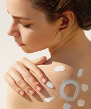 Frau mit aufgetragener Sonnenlotion auf Schulter und Rücken – die Happy Sun Lotion wird gleichmäßig auf der Haut verteilt und symbolisch in Form einer Sonne inszeniert.