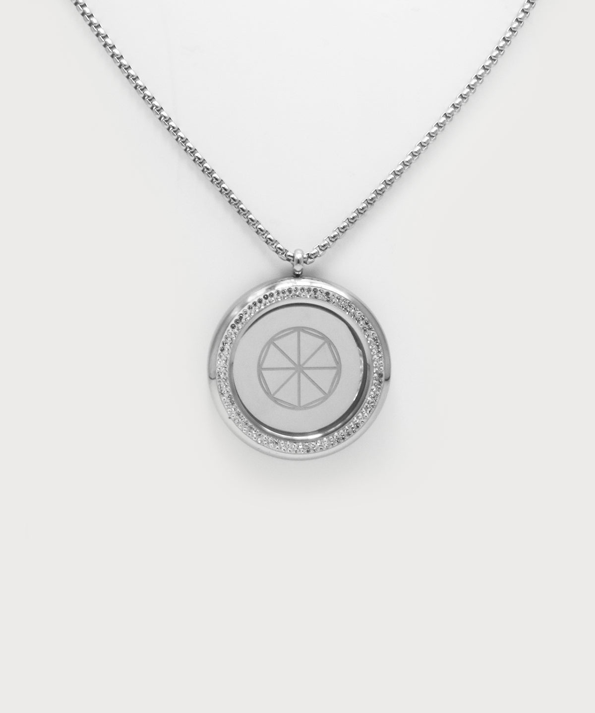 Love & Light Pendant. Silberner Rundanhänger mit feiner Kette, umlaufender Steinbesatz und mit geometrischem Symbol in der Mitte auf hellem Hintergrund.