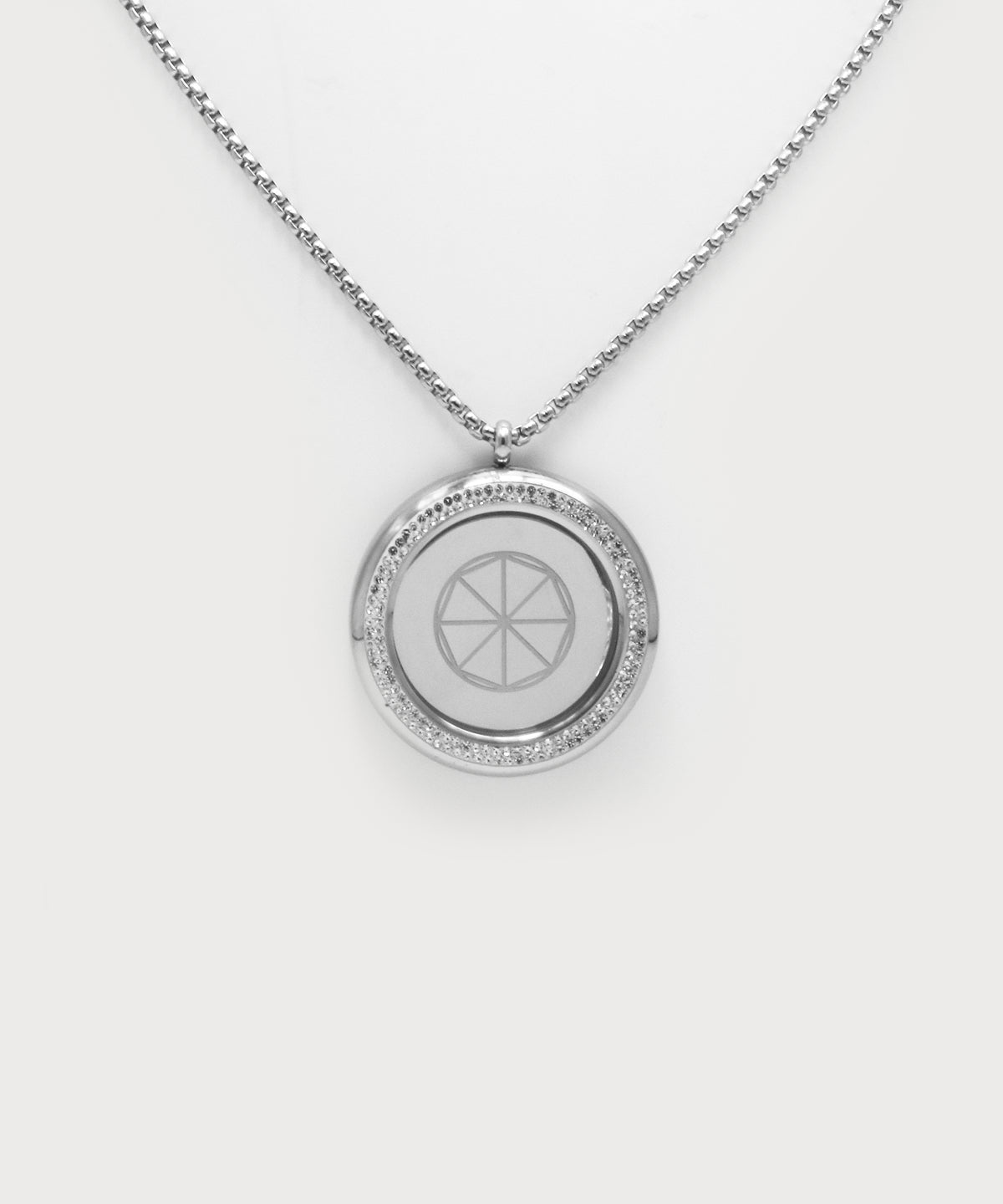 Love & Light Pendant. Silberner Rundanhänger mit feiner Kette, umlaufender Steinbesatz und mit geometrischem Symbol in der Mitte auf hellem Hintergrund.