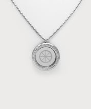 Love & Light Pendant. Silberner Rundanhänger mit feiner Kette, umlaufender Steinbesatz und mit geometrischem Symbol in der Mitte auf hellem Hintergrund.