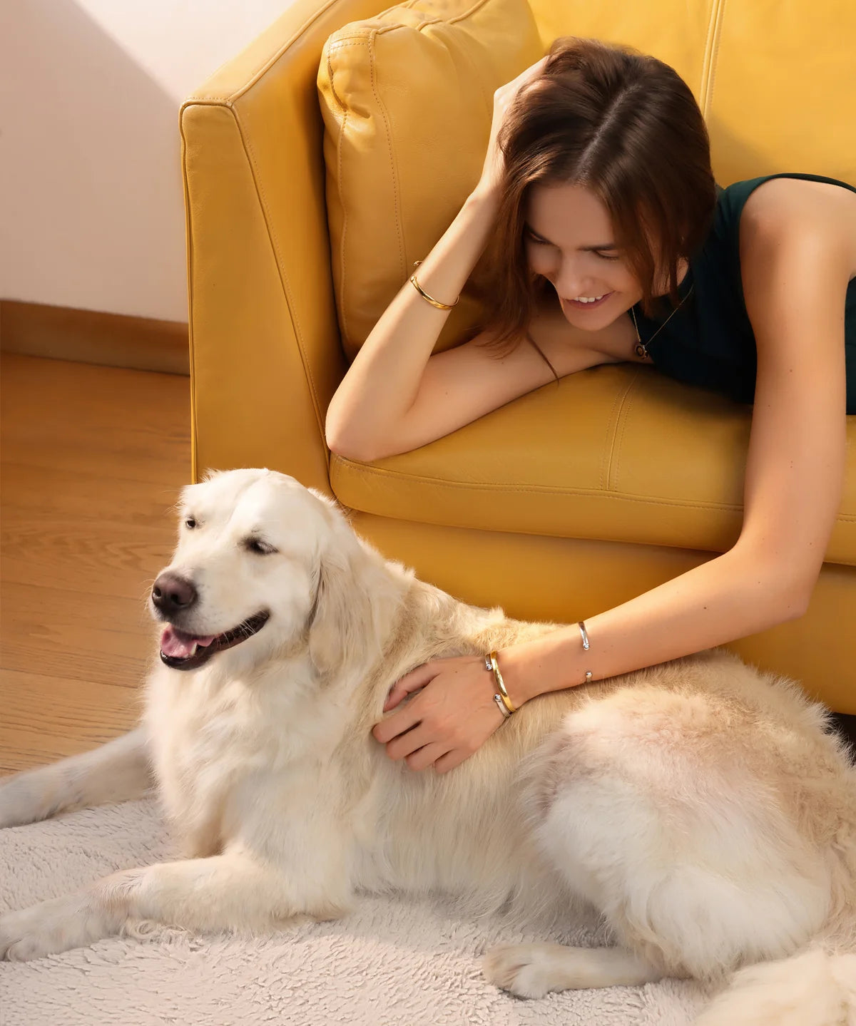 Frau liegt auf einem Sofa im Innenraum, streichelt einen Hund und trägt den Lunara Cuff Armreif in Gold und Silber an den Unterarmen und am linken Handgelenk