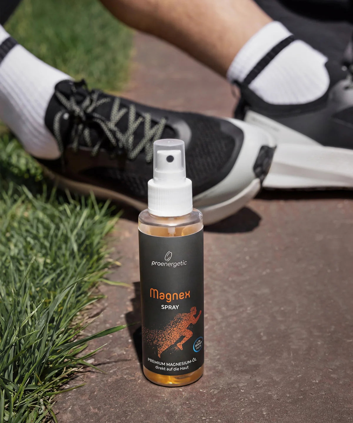 ProEnergetic Magnex Spray standing beside running shoes on a park path, highlighting its use before or after exercise.