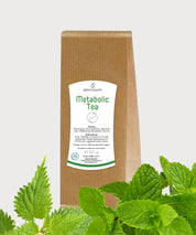 Braune Papierverpackung Metabolic Tea von ProEnergetic mit weißem Etikett, im Vordergrund frische grüne Blätter auf hellem Hintergrund.