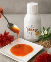 OhMega! 3 Omega Vegan Liquid von proenergetic: Weiße Flasche im Hintergrund, im Vordergrund wird orangefarbenes Omega-3-Liquid von einem Löffel auf einen weißen Teller gegossen; dekoriert mit Pflanzen, Samen und roten Algen als Hinweis auf natürliche Inhaltsstoffe.
