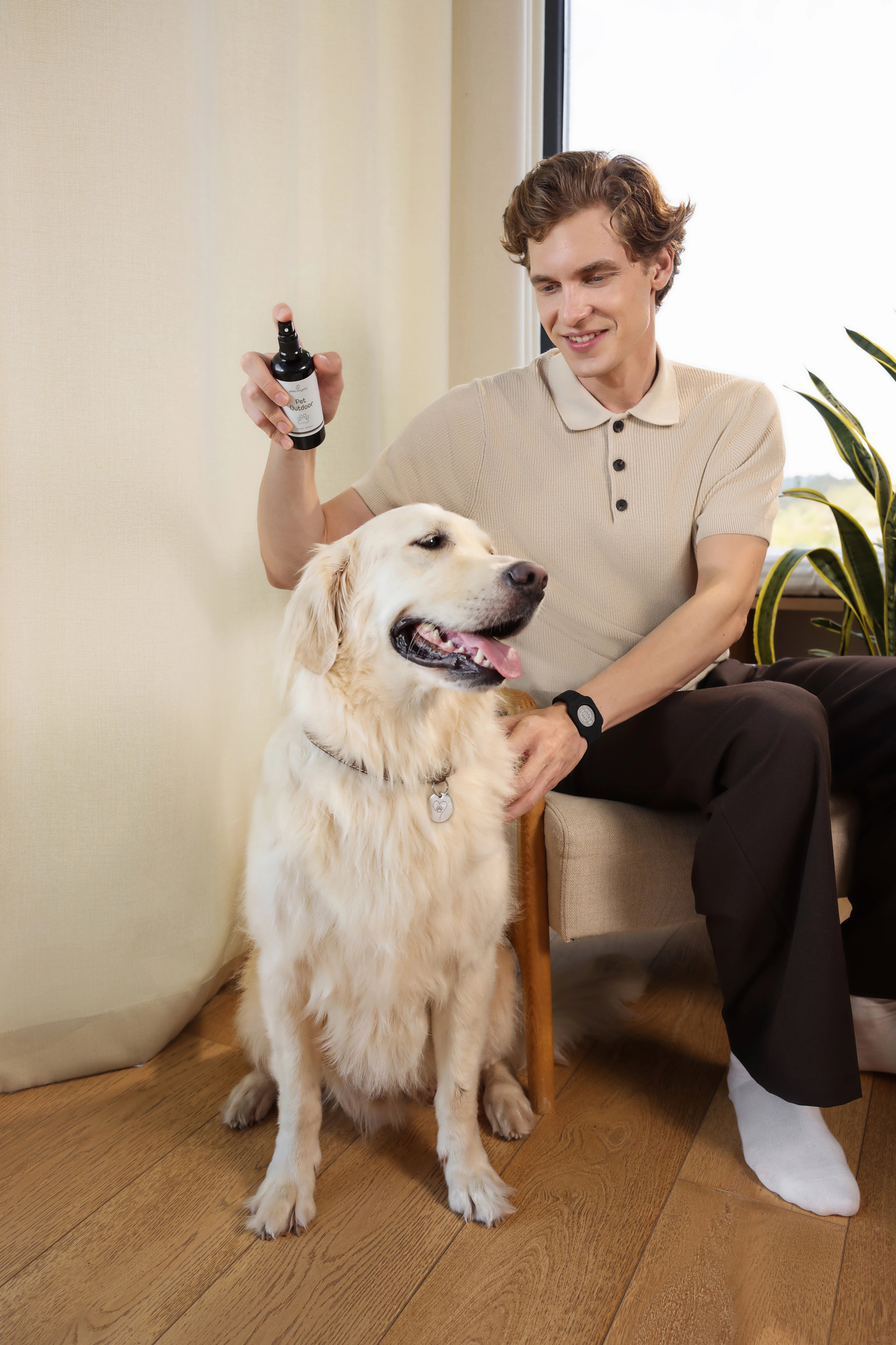 Mann sitzt neben hellem Hund im Wohnraum und hält Pet Outdoor Spray in der Hand, Hund blickt nach vorne.