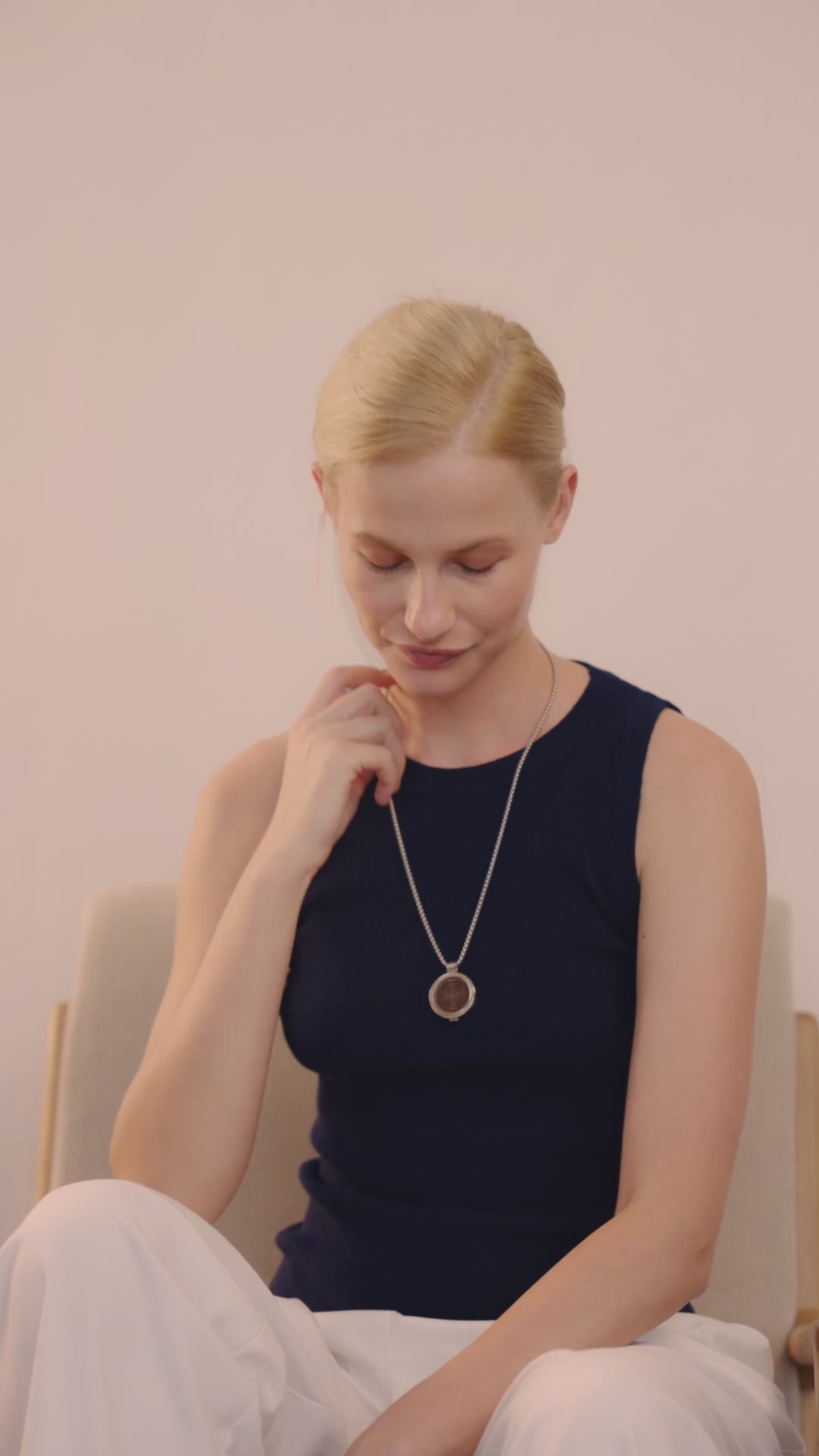 Frau im Innenraum trägt die ProEnergetic KIER Protect Necklace und berührt mit dem runden Anhänger den Kopfbereich