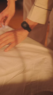 Person liegt schlafend im Bett auf der Seite und trägt ein schwarzes Eloop Band am Handgelenk in warmer Lichtstimmung