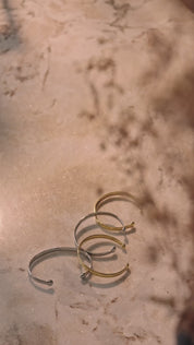 Vier Lunara Cuff Armreifen liegen nebeneinander auf hellbraunem Untergrund in abwechselnder Farbreihenfolge, zwei in Gold und zwei in Silber