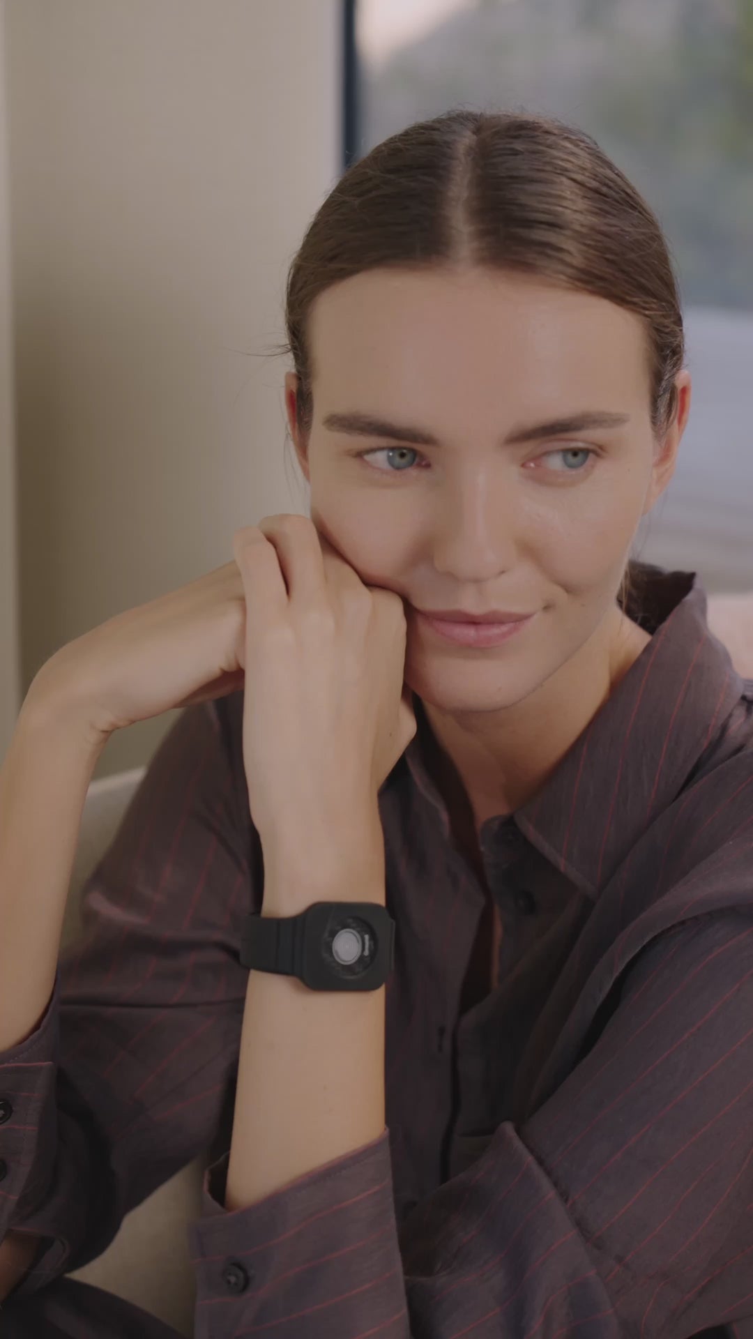 Person sitzt in einem Innenraum, trägt Eloop Band mit Chip, hält das Clearing Spray in der Hand und sprüht es aus der Flasche