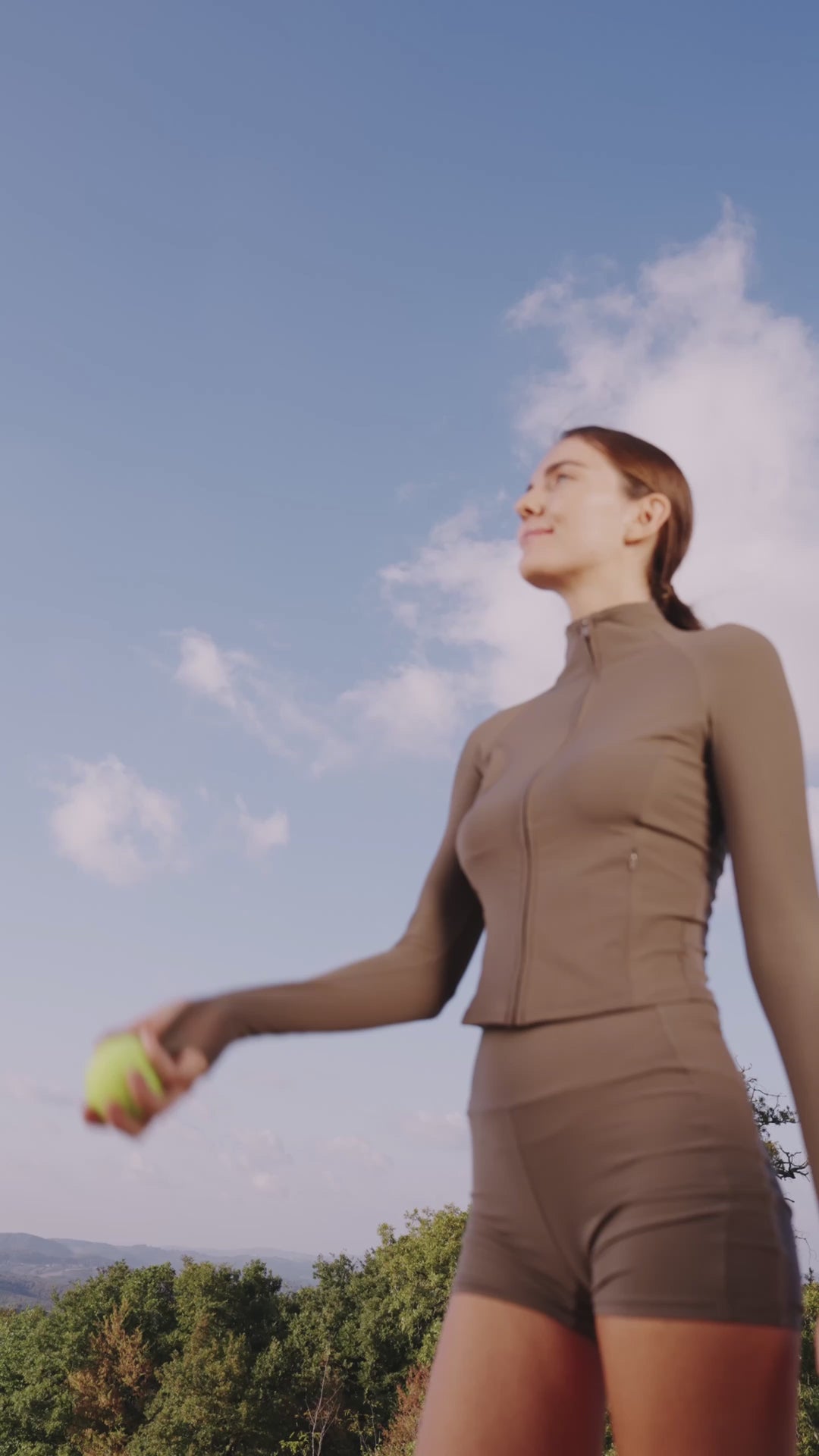 Person steht im Freien in Sportkleidung, spielt mit einem Tennisball und trägt ein oranges Eloop Band Silikonarmband am Handgelenk