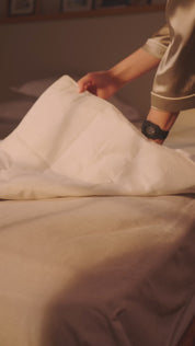 Person legt eine Grounding Sleep Mat unter das Laken auf das Bett und legt sich anschließend zum Schlafen hin