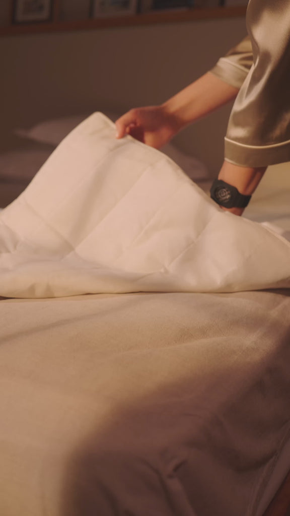 Person legt eine Grounding Sleep Mat unter das Laken auf das Bett und legt sich anschließend zum Schlafen hin