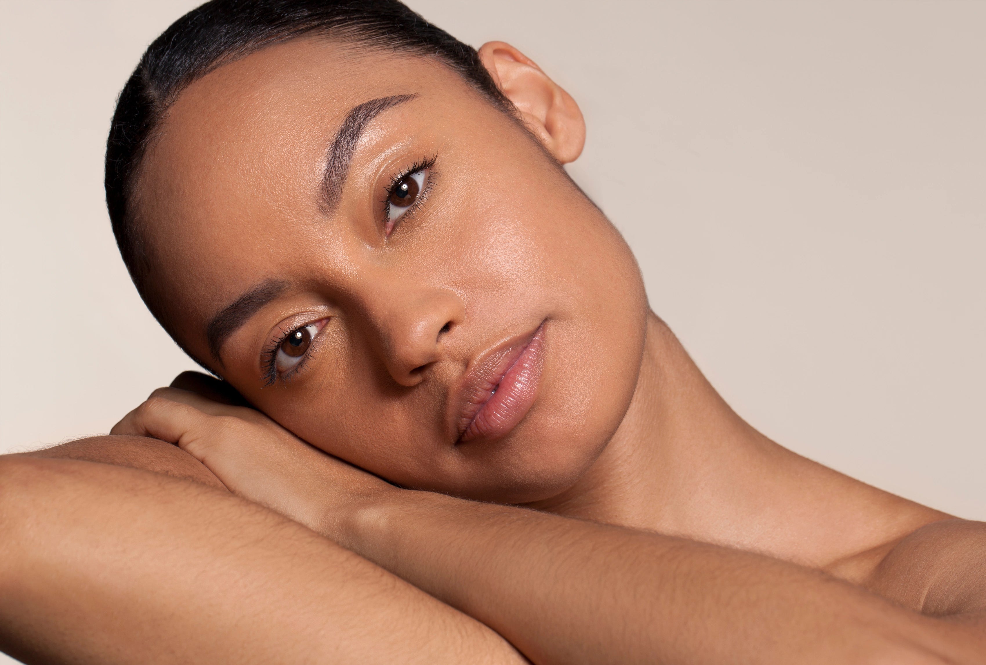 Porträt einer Frau mit glatter, strahlender Haut, die entspannt den Kopf auf den Arm legt; natürlicher Look vor hellem, neutralem Hintergrund – Visual zur Anwendung von „Pure Serum“.