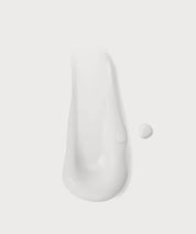 Weiße Cremeprobe in länglicher Form mit kleinem Tropfen auf hellem Hintergrund.