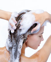Frau beim Haarewaschen mit reichhaltigem, cremigem Schaum – passend zum Repair & Shine Shampoo – während sie das Produkt gründlich in Kopfhaut und Haar einmassiert.