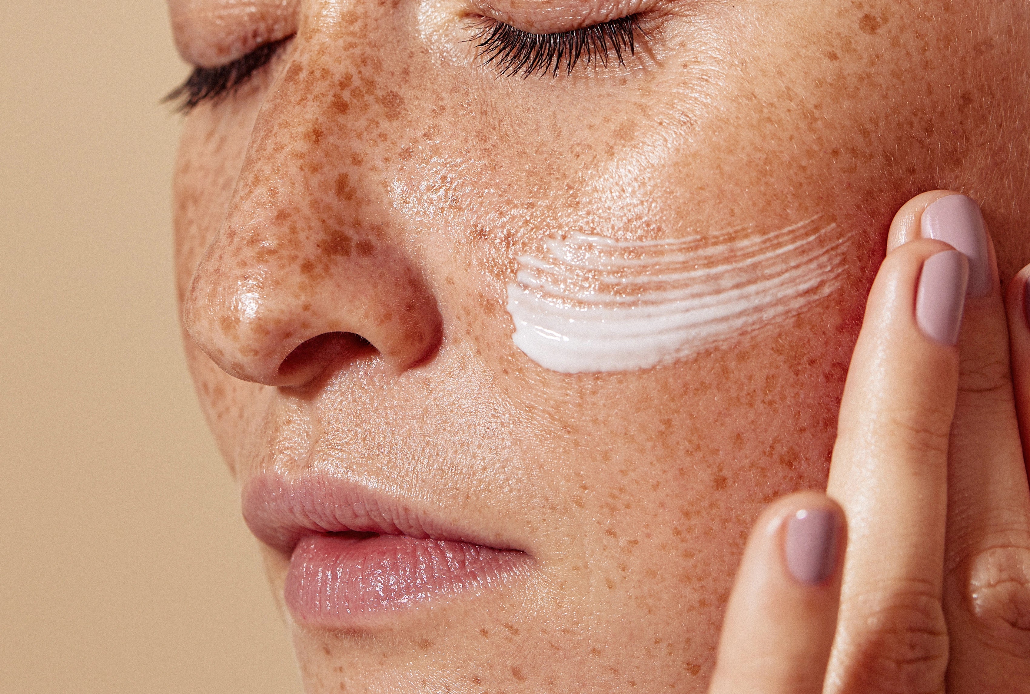 Nahaufnahme eines Gesichts mit aufgetragener weißer Creme auf der Wange und Hand beim Einmassieren.