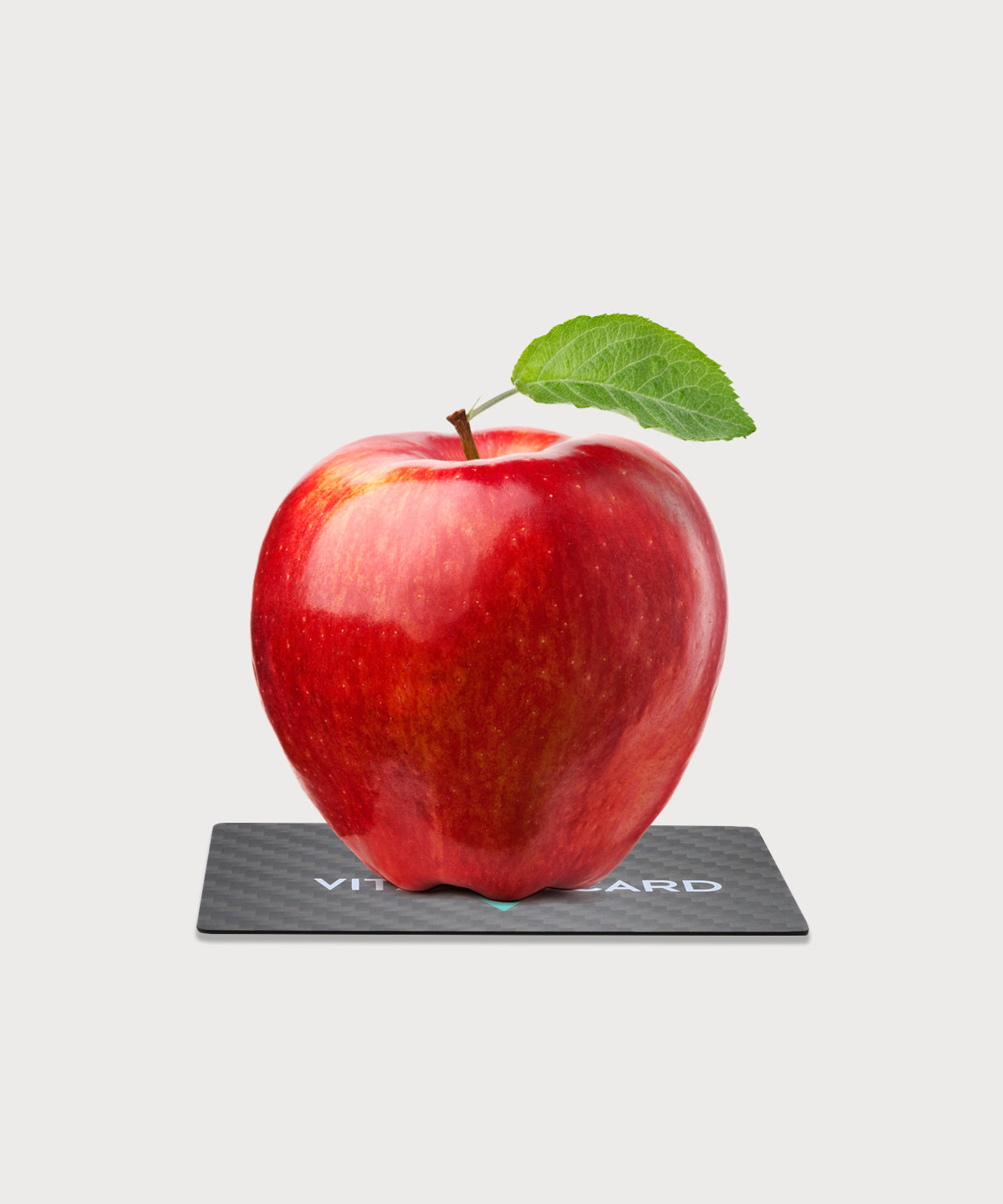 Roter Apfel mit grünem Blatt steht auf der schwarzen Vita Card mit Carbonoptik vor hellem Hintergrund