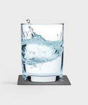Glas mit klarem Wasser steht auf der schwarzen Vita Card mit Carbonoptik, Wasserbewegung im Glas sichtbar