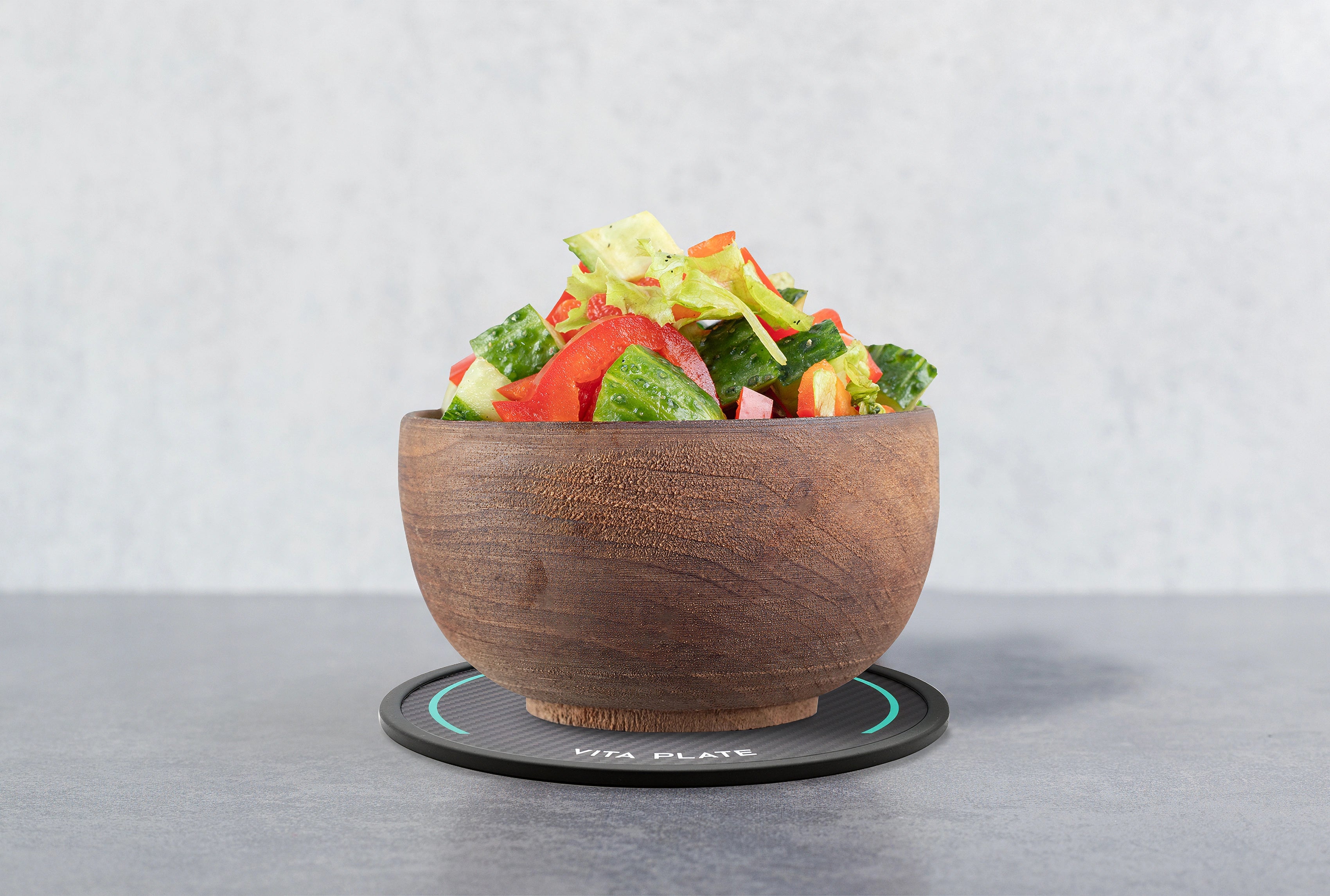 Holzschale mit gemischtem Salat steht auf der runden Vita Plate mit schwarzer Carbonoptik auf grauer Oberfläche